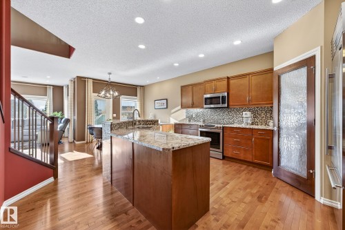 Kitchen featuring wood finish cabinets, light stone counters, a center island with sink, light wood-style flooring, and a textured ceiling - 2036 Hilliard Place, Edmonton, AB - Indoor Photo Showing Kitchen With Upgraded Kitchen