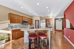Kitchen with a breakfast bar area, wood finish cabinetry, light stone counters, backsplash, and an island with sink - 