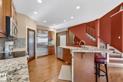 Kitchen featuring wood finish cabinets, a large island with sink, light stone countertops, stainless steel appliances, and light wood-style flooring - 