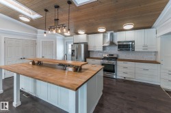 Kitchen with tasteful backsplash, a vaulted wood ceiling, white cabinets, stainless steel appliances, and a skylight - 