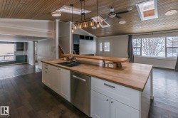 Kitchen with a skylight, white cabinets, a vaulted wooden ceiling, open floor plan, and dark wood-style floors - 