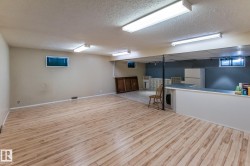 Finished basement with light wood-style flooring, freestanding refrigerator, and a textured ceiling - 