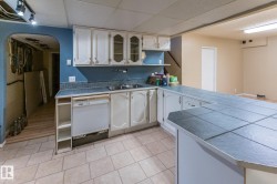 Kitchen featuring tile countertops, open shelves, white cabinets, white dishwasher, and arched walkways - 