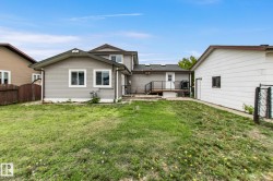Expansive backyard featuring a green lawn, a multi-level deck with black railings, and a detached outbuilding - 