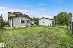 Expansive grassy yard with a two-story home featuring light grey siding and white trim windows - 