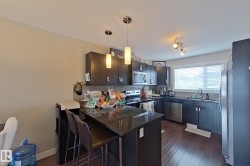 Kitchen with hanging light fixtures, stainless steel appliances, a peninsula, a kitchen bar, and dark wood-type flooring - 