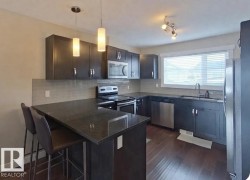 Kitchen with dark stone countertops, stainless steel appliances, a kitchen bar, a peninsula, and decorative light fixtures - 