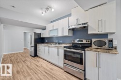 Kitchen featuring appliances with stainless steel finishes, under cabinet range hood, light stone countertops, light wood-style flooring, and a textured ceiling - 