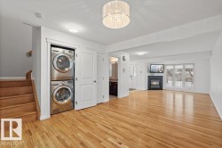 Washroom featuring a textured ceiling, light wood-style flooring, stacked washer and clothes dryer, a chandelier, and a glass covered fireplace - 