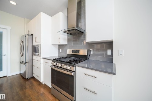 Kitchen with stainless steel appliances, white cabinetry, dark wood-style floors, dark stone counters, and recessed lighting - 19743 26 Avenue, Edmonton, AB - Indoor Photo Showing Kitchen With Upgraded Kitchen