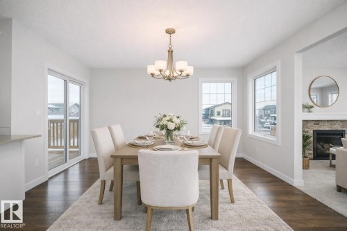 Dining area featuring dark wood-style flooring, suspended lighting, a stone fireplace, and plenty of natural light - 19743 26 Avenue, Edmonton, AB - Indoor Photo Showing Dining Room With Fireplace