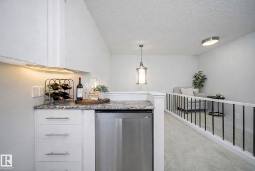 Kitchen featuring stainless steel dishwasher, white cabinetry, a textured ceiling, decorative light fixtures, and light carpet - 19743 26 Avenue, Edmonton, AB - Indoor