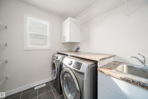 Laundry room with dark tile patterned flooring, washing machine and clothes dryer, and cabinet space - 19743 26 Avenue, Edmonton, AB - Indoor Photo Showing Laundry Room