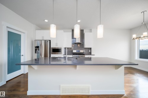 Kitchen with a kitchen bar, white cabinetry, stainless steel appliances, and dark wood finished floors - 19743 26 Avenue, Edmonton, AB - Indoor Photo Showing Kitchen With Upgraded Kitchen