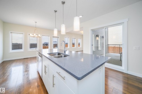 Kitchen with white cabinetry, dark wood-style flooring, dark stone countertops, and a chandelier - 19743 26 Avenue, Edmonton, AB - Indoor Photo Showing Kitchen With Double Sink