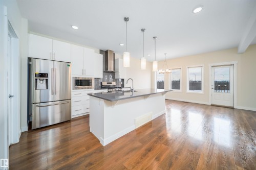 Kitchen featuring stainless steel appliances, a kitchen breakfast bar, white cabinetry, dark wood-type flooring, and a chandelier - 19743 26 Avenue, Edmonton, AB - Indoor Photo Showing Kitchen With Upgraded Kitchen