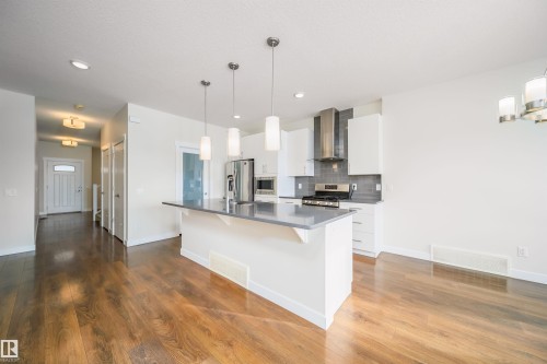 Kitchen featuring white cabinetry, a breakfast bar area, stainless steel appliances, dark wood finished floors, and backsplash - 19743 26 Avenue, Edmonton, AB - Indoor Photo Showing Kitchen With Upgraded Kitchen