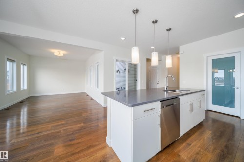 Kitchen featuring open floor plan, white cabinetry, stainless steel dishwasher, hanging light fixtures, and dark wood finished floors - 19743 26 Avenue, Edmonton, AB - Indoor Photo Showing Kitchen With Upgraded Kitchen