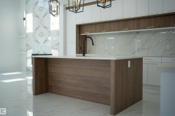 Kitchen featuring two tone cabinets, an island with sink, a chandelier, light stone counters, and modern cabinets - 