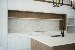 Kitchen with two tone color scheme, light stone counters, modern cabinets, tasteful backsplash, and hanging lights - 