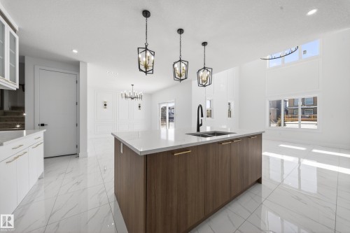Kitchen with modern cabinets, a kitchen island with sink, glass fronted cabinets, light stone countertops, and two tone color scheme - 4006 40 Street, Beaumont, AB - Indoor Photo Showing Kitchen With Double Sink