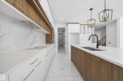 Two tone kitchen featuring two tone cabinets, modern cabinets, light stone countertops, glass insert cabinets, and hanging lights - 