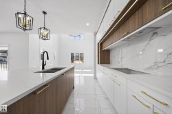 Dual tone kitchen featuring two tone cabinetry, modern cabinets, light stone counters, light marble finish floors, and a chandelier - 