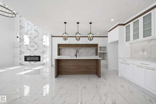 Dual tone kitchen featuring a chandelier, two tone cabinets, a fireplace, modern cabinets, and light stone counters - 4006 40 Street, Beaumont, AB - Indoor