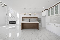 Dual tone kitchen featuring a chandelier, two tone cabinets, a fireplace, modern cabinets, and light stone counters - 