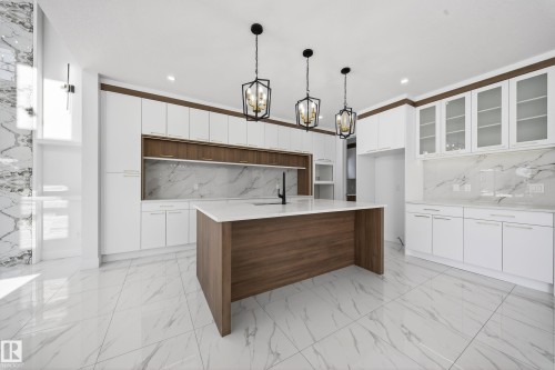 Kitchen featuring light marble finish floors, light stone countertops, a kitchen island with sink, suspended lighting, and glass insert cabinets - 4006 40 Street, Beaumont, AB - Indoor