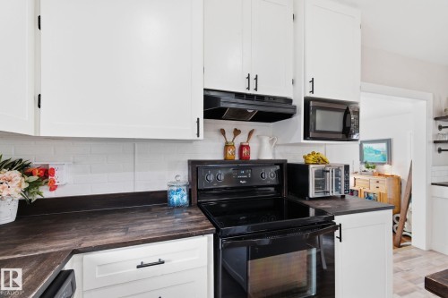 Kitchen featuring dark countertops, black range with electric cooktop, white cabinets, tasteful backsplash, and light wood-style flooring - 4919 50 Avenue, Bon Accord, AB - Indoor Photo Showing Kitchen