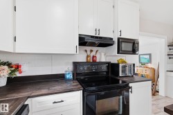 Kitchen featuring dark countertops, black range with electric cooktop, white cabinets, tasteful backsplash, and light wood-style flooring - 