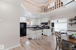 Kitchen with white cabinets, black appliances, a kitchen breakfast bar, a center island, and dark countertops - 