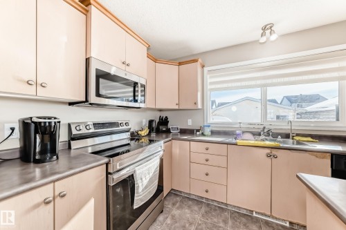 Kitchen with stainless steel appliances, stainless steel counters, light wood finish cabinetry, cream cabinetry, and light tile patterned floors - 14043 151 Avenue, Edmonton, AB - Indoor Photo Showing Kitchen With Double Sink