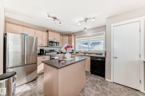 Kitchen featuring stainless steel appliances, a center island, dark countertops, light tile patterned floors, and a textured ceiling - 14043 151 Avenue, Edmonton, AB - Indoor Photo Showing Kitchen With Double Sink