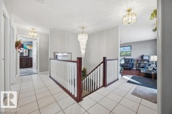 Corridor featuring suspended lighting, an upstairs landing, and light tile patterned floors - 