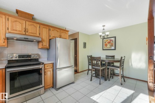 Kitchen with stainless steel appliances, light countertops, backsplash, suspended lighting, and light tile patterned floors - 760 Knottwood Road S, Edmonton, AB - Indoor Photo Showing Kitchen