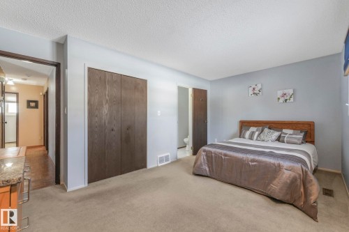 Carpeted bedroom with a textured ceiling, a closet, and ensuite bath - 760 Knottwood Road S, Edmonton, AB - Indoor Photo Showing Bedroom
