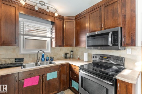 Kitchen with stainless steel appliances, decorative backsplash, light countertops, and wood finish cabinets - 9847 79 Street, Edmonton, AB - Indoor Photo Showing Kitchen With Double Sink