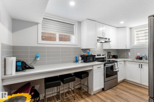 Kitchen featuring stainless steel appliances, white cabinets, light wood-type flooring, backsplash, and a textured ceiling - 9847 79 Street, Edmonton, AB - Indoor Photo Showing Kitchen With Upgraded Kitchen