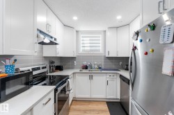 Kitchen with stainless steel appliances, white cabinetry, decorative backsplash, a textured ceiling, and light wood-style flooring - 