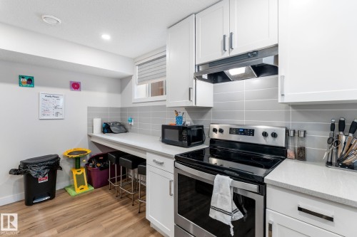Kitchen with stainless steel range with electric stovetop, white cabinetry, decorative backsplash, black microwave, and light wood finished floors - 9847 79 Street, Edmonton, AB - Indoor Photo Showing Kitchen