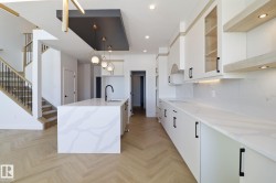 Kitchen with light stone countertops, a center island with sink, white cabinetry, parquet floors, and decorative light fixtures - 