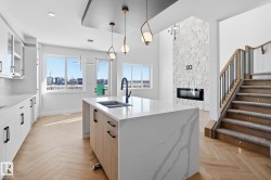 Two tone kitchen featuring a stone fireplace, glass insert cabinets, decorative light fixtures, a kitchen island with sink, and light stone counters - 