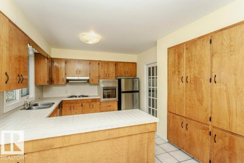 Kitchen featuring tile counters, a peninsula, stainless steel appliances, and wood finish cabinets - 6304 131 Street, Edmonton, AB - Indoor Photo Showing Kitchen With Double Sink