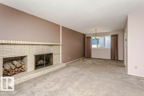 Unfurnished living room with a brick fireplace, carpet flooring, a textured ceiling, and suspended lighting - 6304 131 Street, Edmonton, AB - Indoor Photo Showing Living Room With Fireplace
