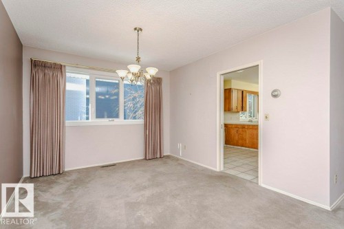 Unfurnished room featuring hanging lights, light colored carpet, and a textured ceiling - 6304 131 Street, Edmonton, AB - Indoor