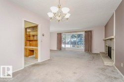 Unfurnished living room featuring a textured ceiling, light colored carpet, a chandelier, and a brick fireplace - 