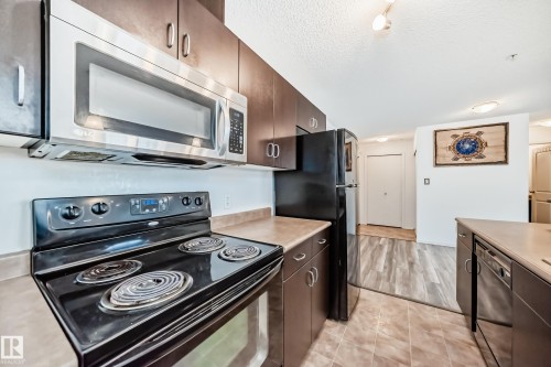 Kitchen with black appliances, dark wood finish cabinets, light countertops, and a textured ceiling - 306 1188 Hyndman Road, Edmonton, AB - Indoor Photo Showing Kitchen