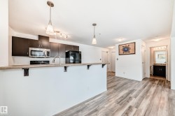Kitchen featuring decorative light fixtures, black appliances, a breakfast bar area, light countertops, and light wood finished floors - 